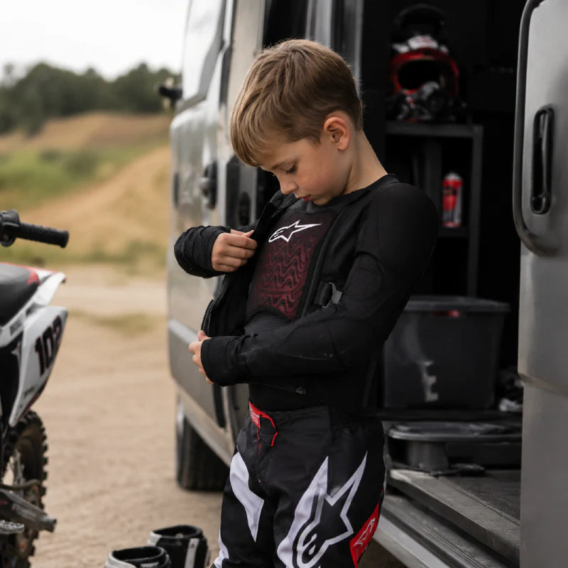 Een jonge crosser trekt zijn Alpinestars bodyvest aan die goed gekeurd is voor KNMV wedstrijden.