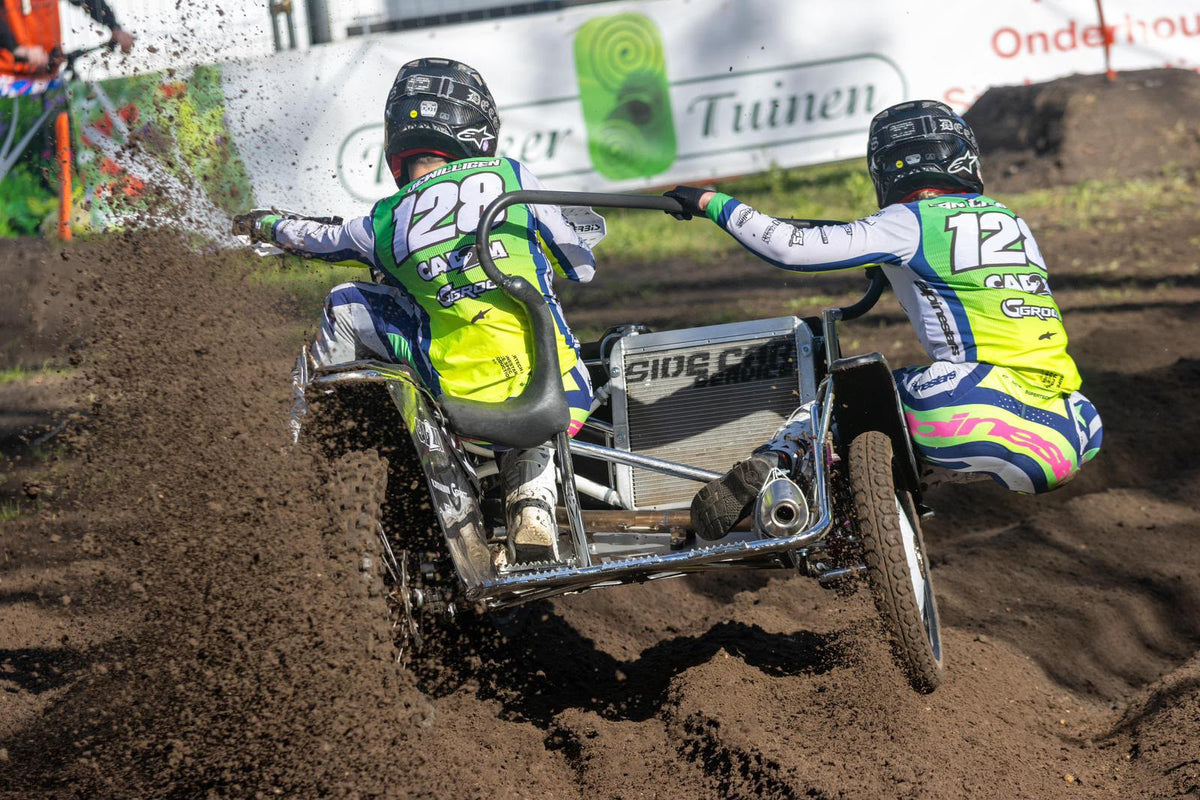 Een zijspan duo in actie in de bocht waarbij het binnenste wiel loskomt van de grond en de bagger spuit van het achterwiel. Het duo draagt slimfit speciale made crossshirts die zelf ontworpen zijn op basis van de Alpinestars supertech kleding.